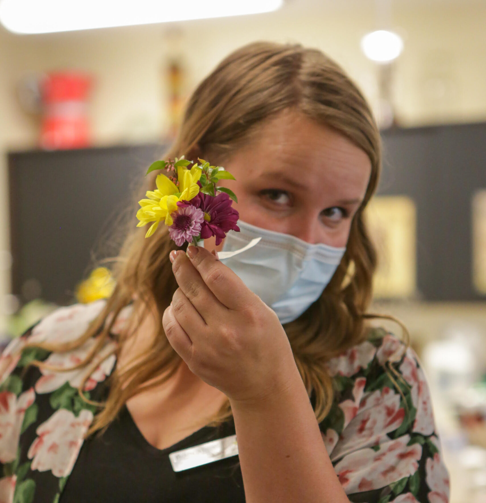 a horticultural therapist holding up a bouquet, at work wearing a mask